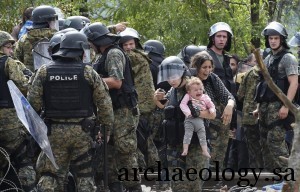 epa04893063 A member of the Macedonian special police forces holds a baby as migrants try to cross into Macedonia near the southern city of Gevgelija, The Former Yugoslav Republic of Macedonia, 22 August 2015. Macedonian security forces strengthened the barricades along the Greek border 22 August, where thousands of refugees from the Middle East were stranded after a hot day and a rainy, chilly night, local media reported.  EPA/GEORGI LICOVSKI
